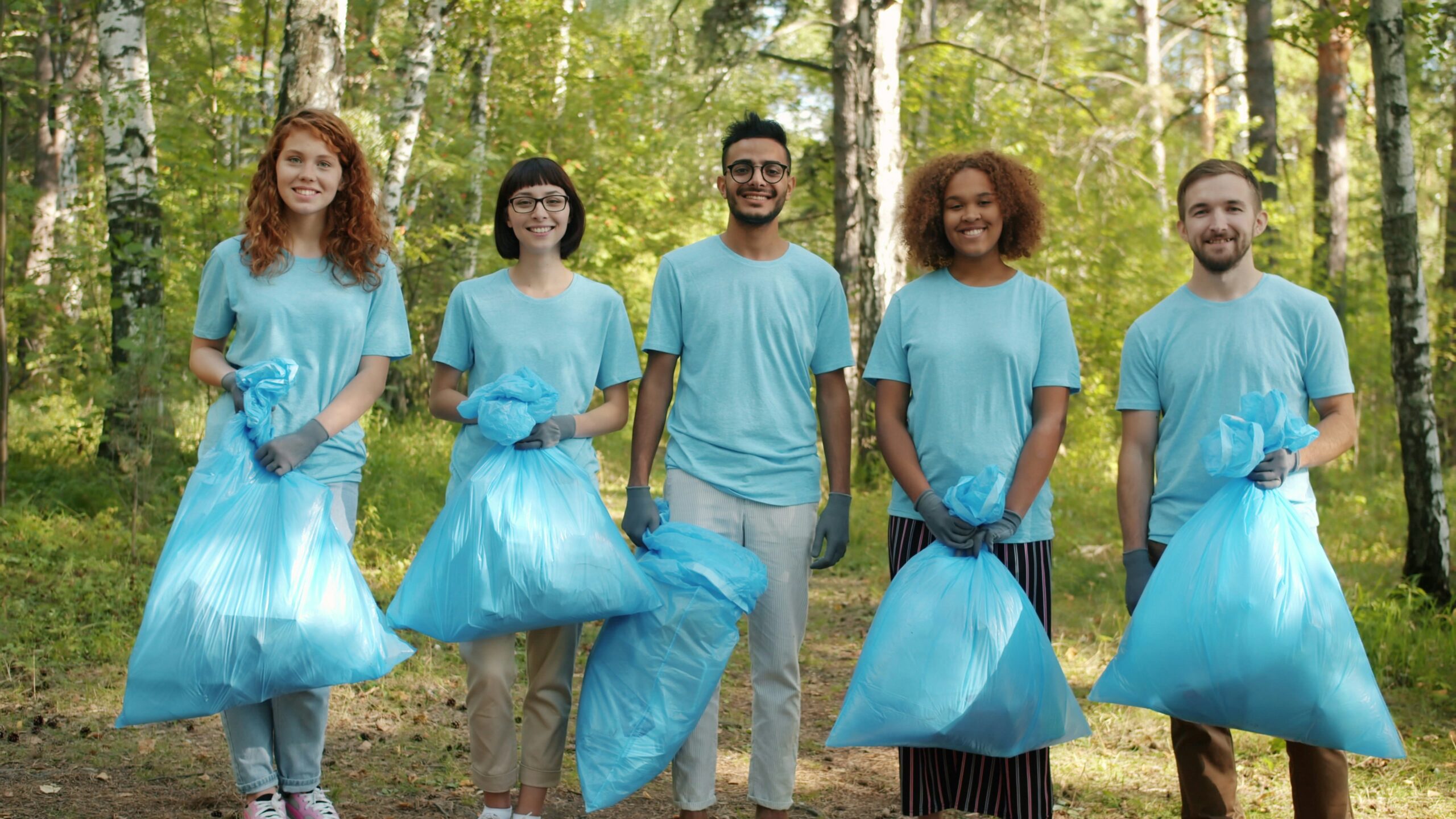 A small group of volunteers with trash bags and pickers preparing to organize a litter pick in a forest.